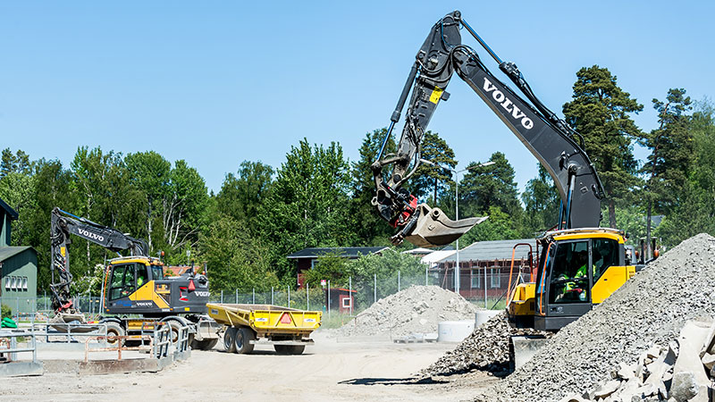 Grävmaskiner bland stora grushögar.