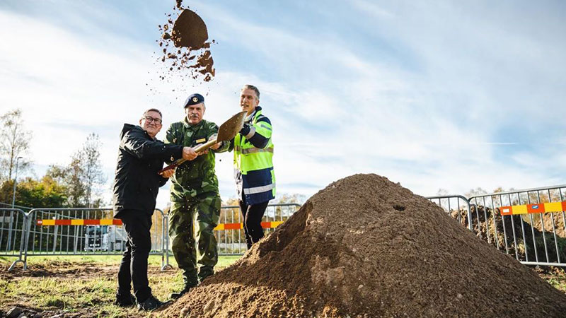 Tre män kastar sand i luften med en gemensam spade.