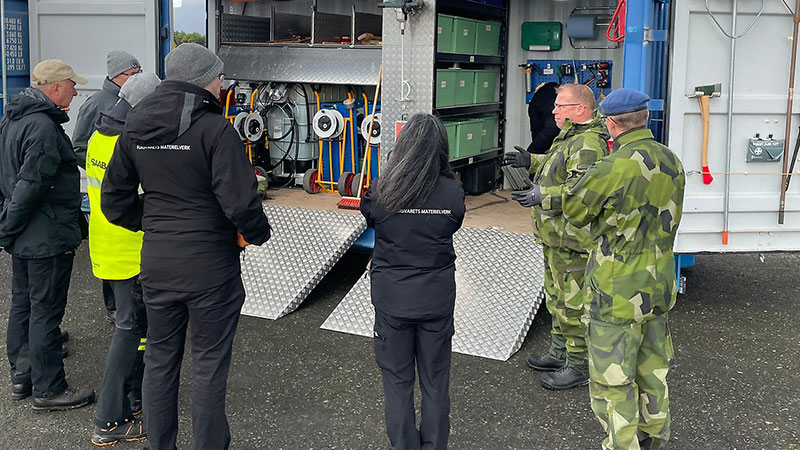 Flera personer står och tittar in i en container fylld med prylar