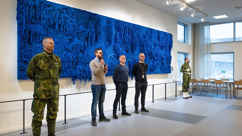 Män på rad framför ett blått konstverk på väggen