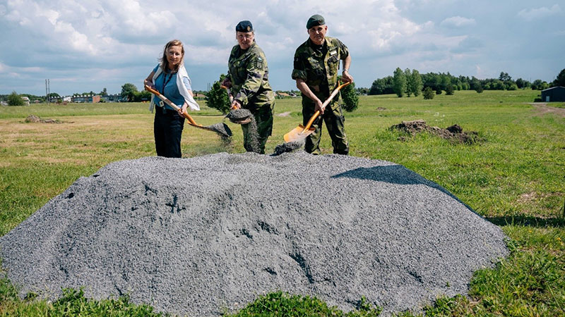 Tre personer står på rad med en varsin spade redo att gräva i en grushög