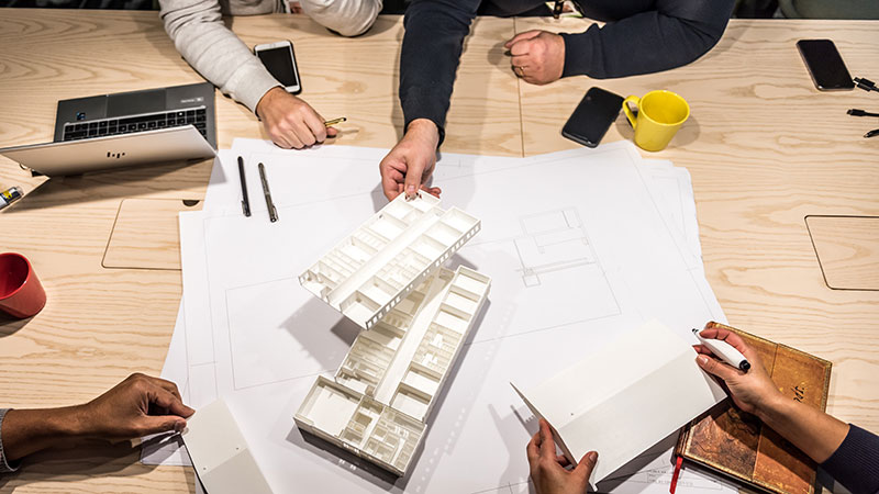 3D-modell av en byggnad står på ett mötesbord runtomkring sitter flera personer. 
