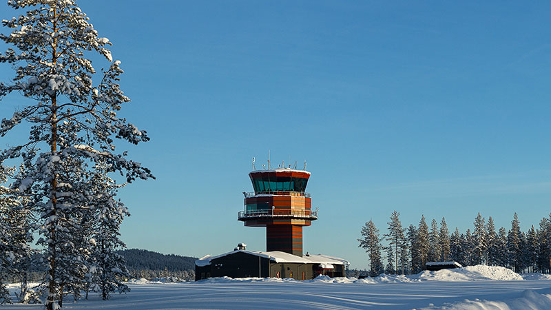 Röd- och grårandigt flygledtartorn som kommer upp en en låg gråmålad byggnad. 