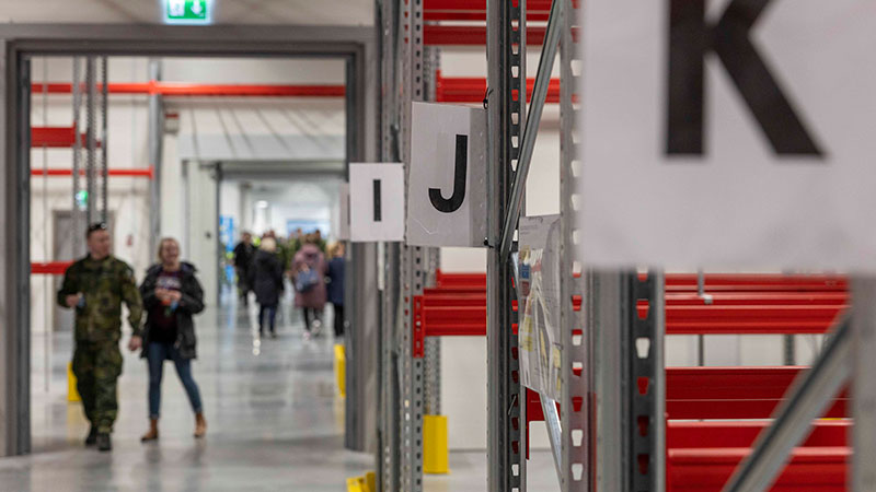 Interiör med stallage märkta med bokstäver och några människor i bakgrunden