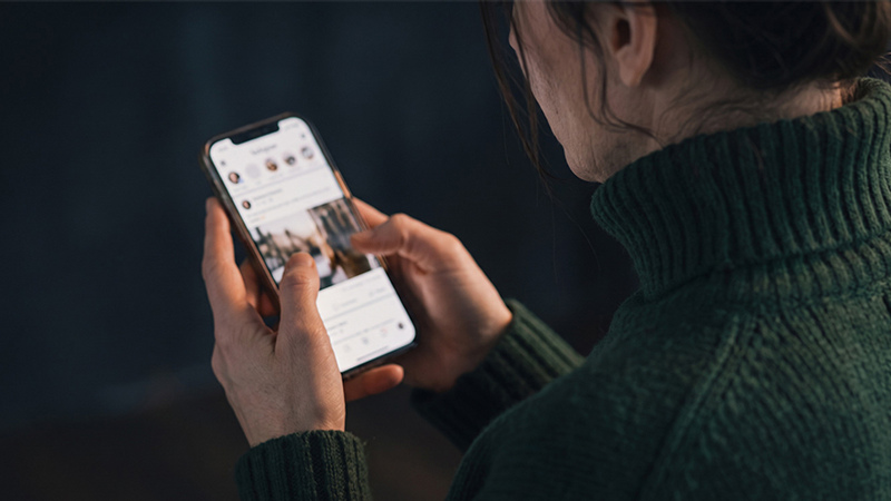 Kvinna sitter med en mobiltelefon i handen med sidan mot betraktaren