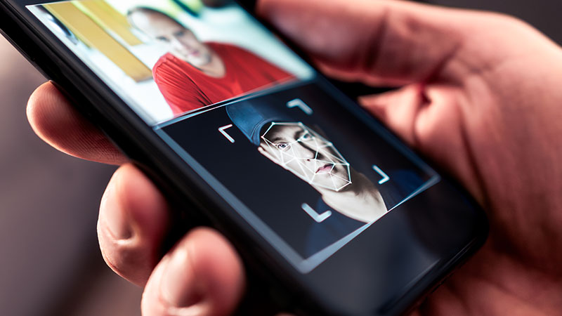 hand som håller mobiltelefon där det är en pågående deepfejk med två olika ansikten