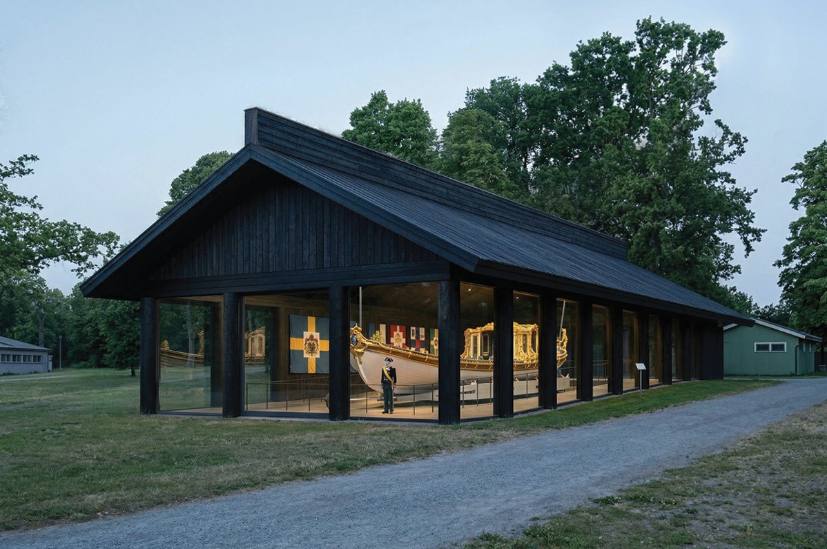 En träbyggnad med stora glaspartier. Inne i byggnaden syns en rikt dekorerad båt.