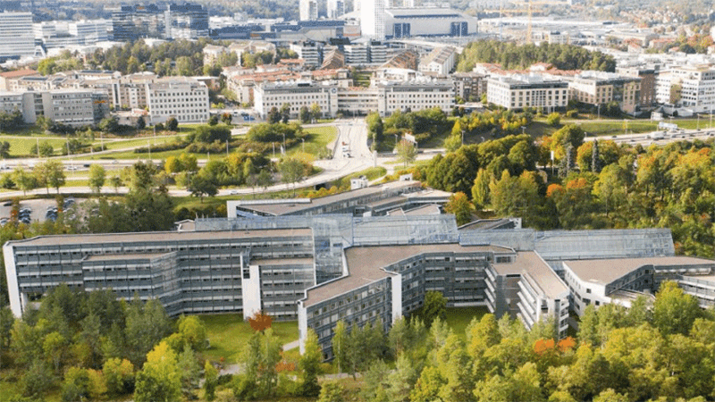 Översiktsbild på fastigheten från luften visar en vit långsmal byggnad