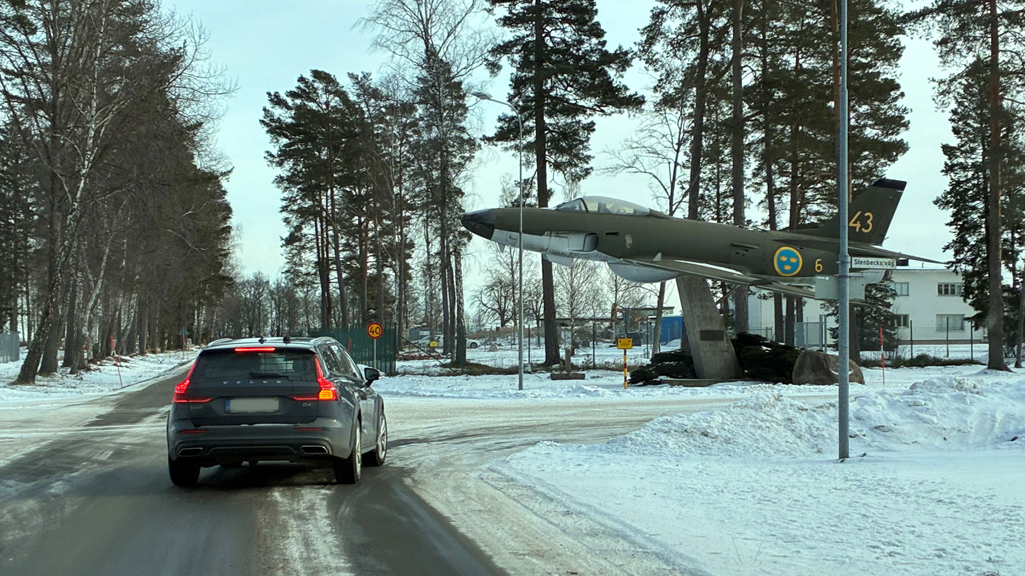 En svart bil på en väg framför ett monument av ett militärflygplan