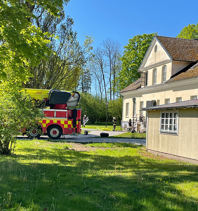 Brandbil står uppbackad mot en herrgård i ljus färg. Ingen eld syns.